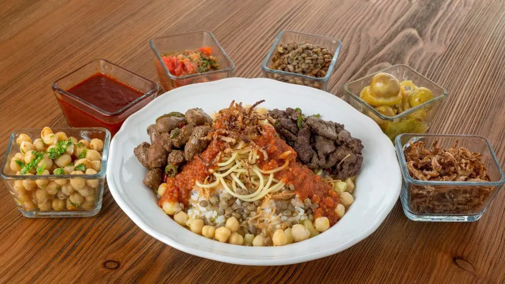 Koushari egyptian food with chicken liver and beef kebab chickpea noodles boiled rice lentil fried onion tomato chili sauce and pickle served in dish isolated on table top view