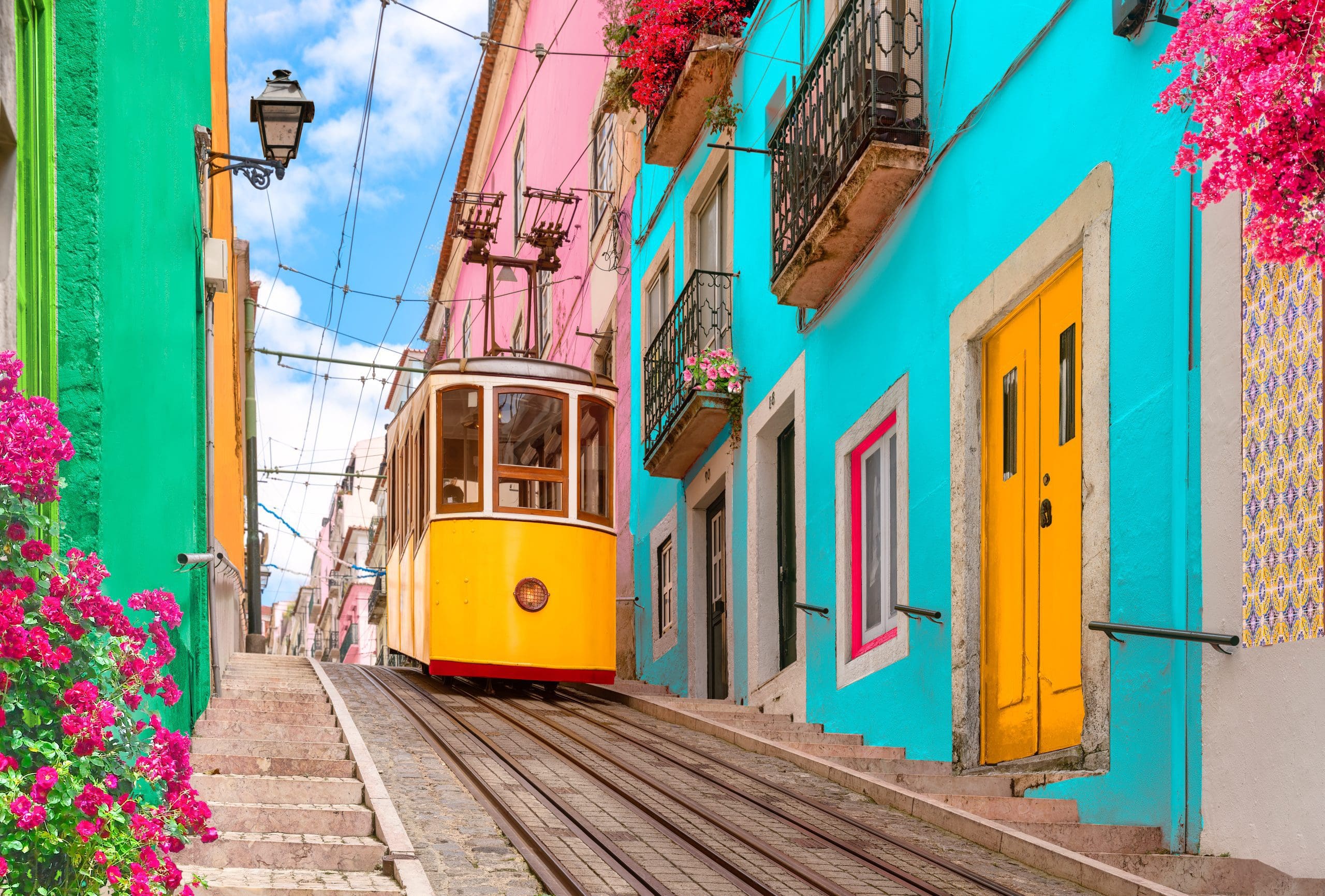 Yellow electric tram on a street with colorful houses and flowers on the balconies - Bica Elevator going down the hill of Chiado in Lisbon, Portugal.