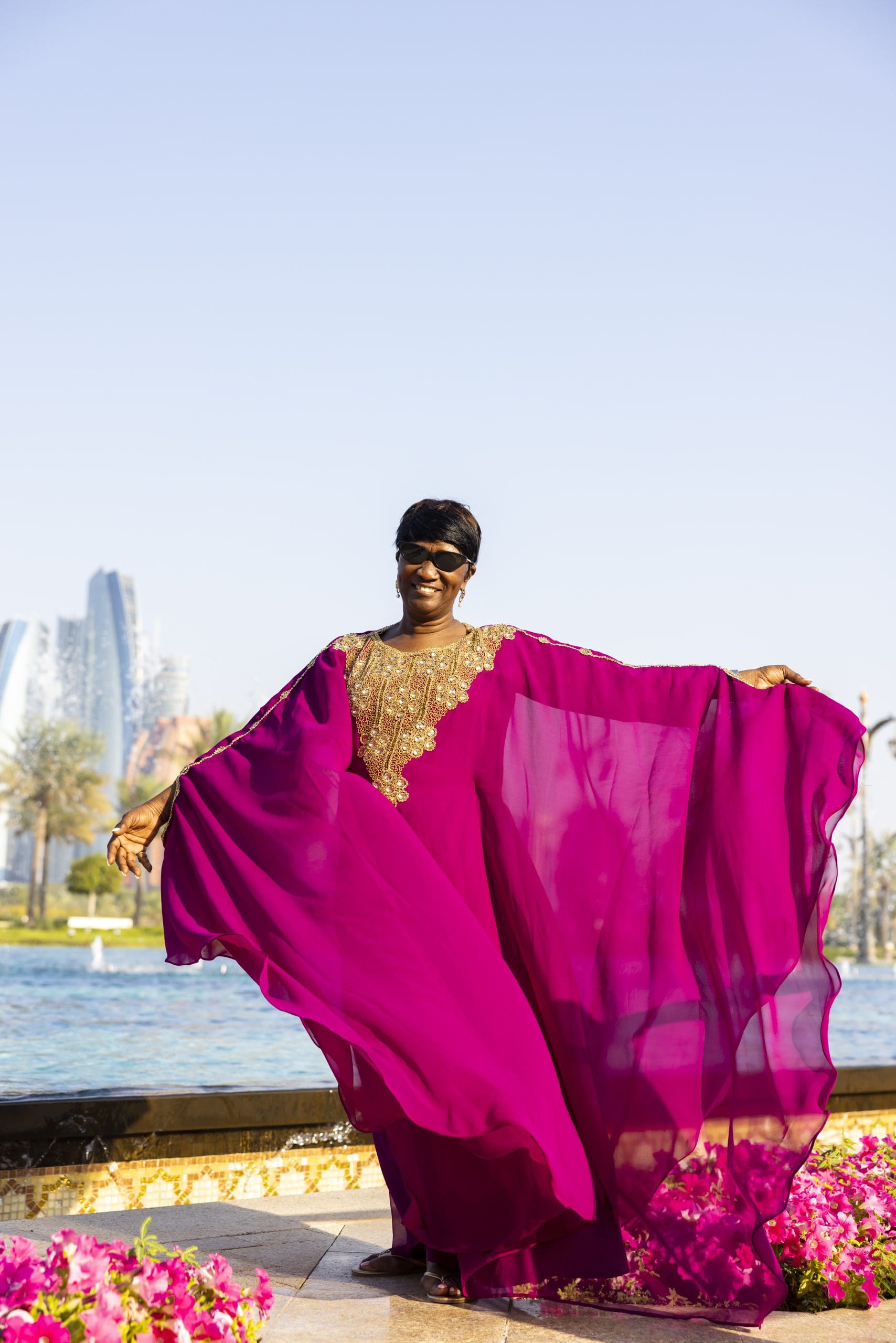 Black woman in magenta kaftan in front of Dubai landscape