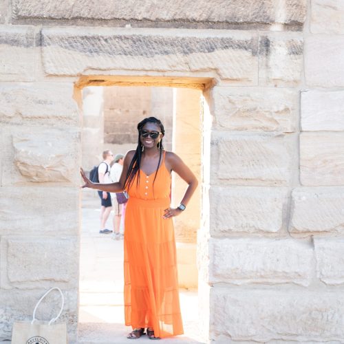 Black woman (travel diva) in the door way of a Egyptian monument with orange flowy dress.