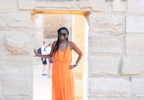 Black woman (travel diva) in the door way of a Egyptian monument with orange flowy dress.
