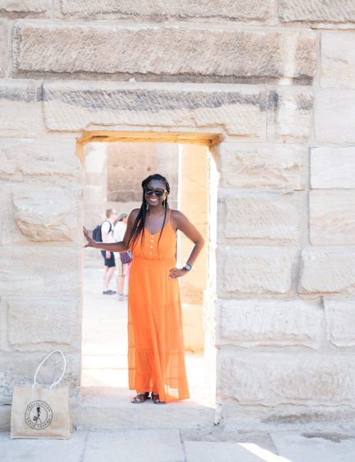 Black woman (travel diva) in the door way of a Egyptian monument with orange flowy dress.