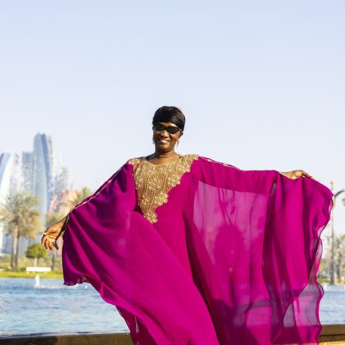 Black woman in magenta kaftan in front of Dubai landscape