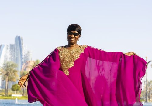 Black woman in magenta kaftan in front of Dubai landscape